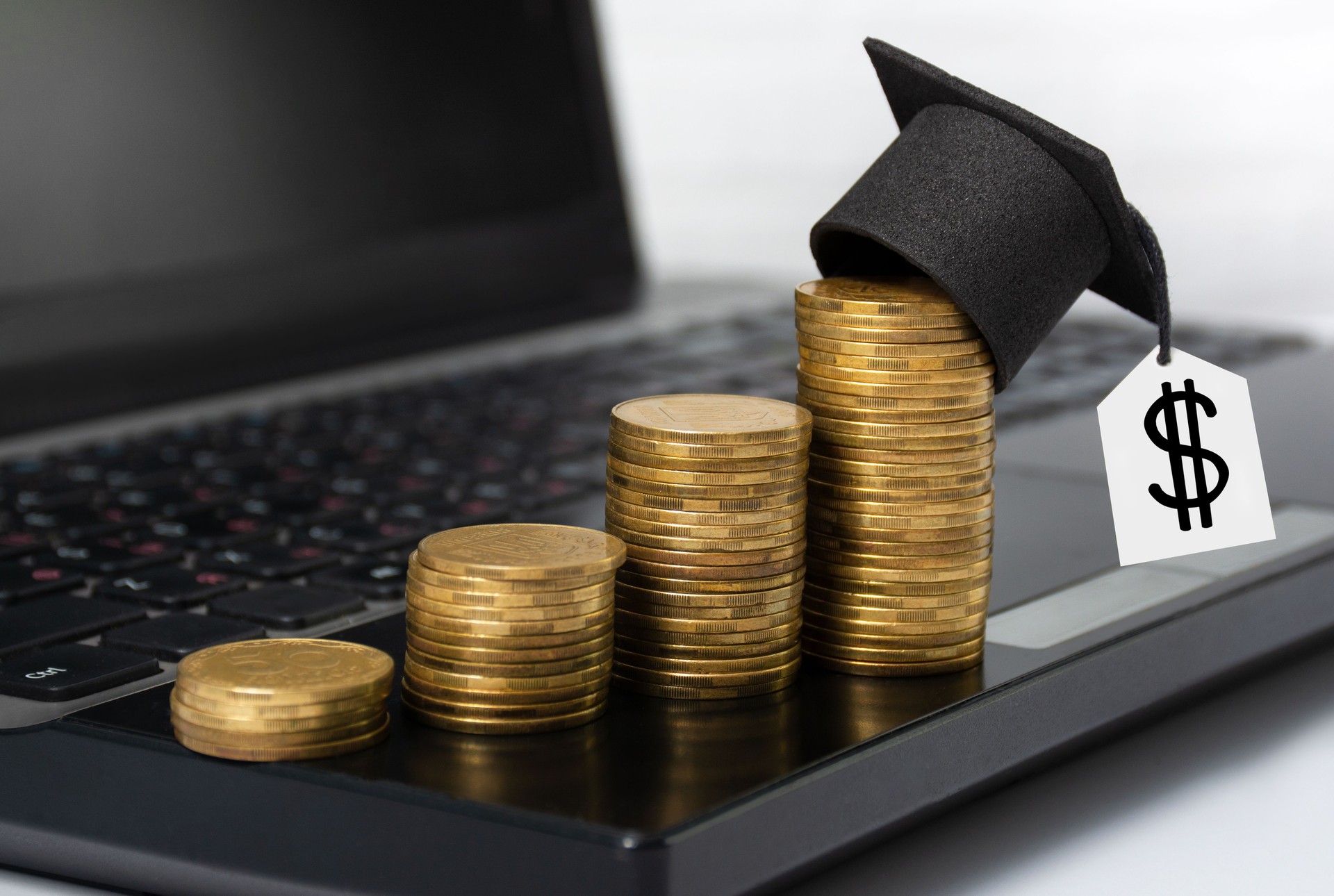 Concept of financial literacy and education. Gold coins with graduation hat stand on laptop on desktop